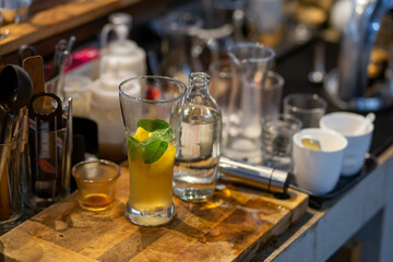 A close-up of a lemon-soda cold drink in a clear glass on the cafe table where the barista is mixing something into the glass. Summer refreshing drink