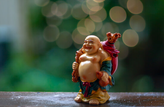 Happy llaugh buddha statue standing on wooden shelf with defocus background.