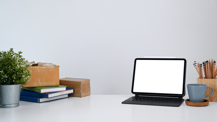 Modern workplace with mock up computer tablet, house plant and books on white desk.