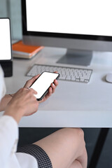 Cropped shot of businesswoman working with multiple devices and holding smartphone while sitting at office.