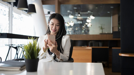 Fototapeta na wymiar Beautiful businesswoman using smart phone and listening music in earphones at office.