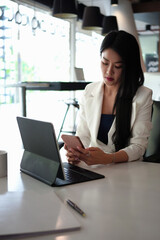 Portrait of businesswoman checking mobile phone and working with computer tablet in office.