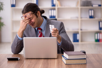 Young sick male employee sitting at workplace