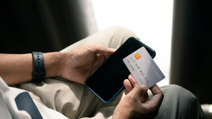 Close up view of man holding credit card and using smart phone for online payment or online shopping.