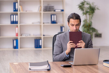 Young male employee student reading book at workplace