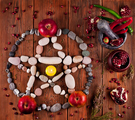 Pentagram made of stones with pomegranate, apples, red and green hot chili peppers, dry heather branches on a wooden background. Top view.