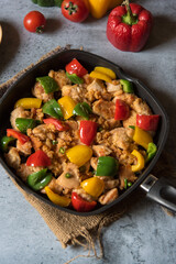 Chicken pieces and bell peppers in a black pan with use of selective focus.
