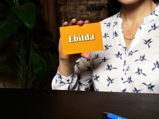 Woman's hand showing orange business card with phrase Ebitda - closeup shot on grey background