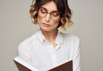 Woman with a notepad in her hands and wearing glasses on a gray background cropped view of a Light shirt
