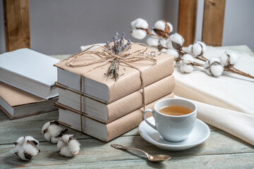 Cute stack of books with craft paper covers, wrapped in rope and decorated with lavender flowers, and a cup of tea on a wooden table