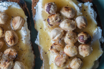 Two bread toast with cream cheese, roasted hazelnuts, honey, pepper and salt, close up, top view