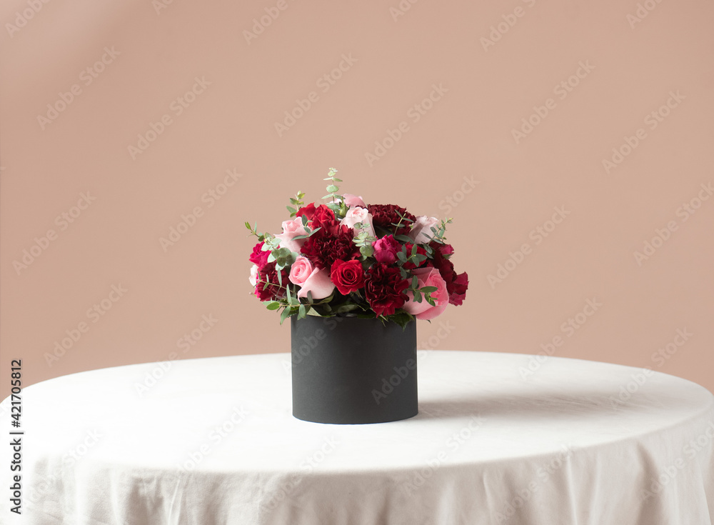 Wall mural red, pink and dark red roses bouquet in a black box on a white table and pink backround