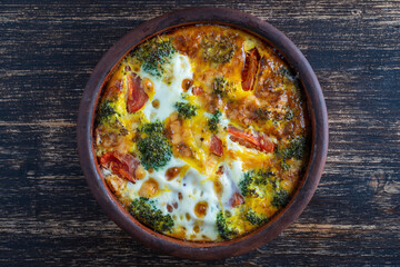 Frittata with egg, tomato, pepper, onion, broccoli and cheese on wooden table. Italian egg omelette