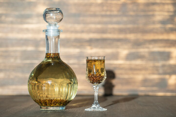 Homemade birch buds tincture in a glass bottle and a wine crystal glass on a wooden table background