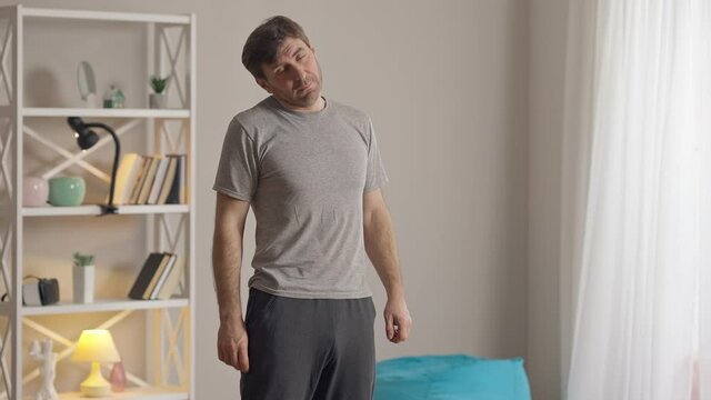 Middle shot of concentrated man stretching neck exercising at home in the morning. Portrait of confident fit Caucasian sportsman training indoors. Workout and healthy lifestyle concept.