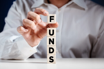 Businessman places a cube on top of tiered wooden cubes with the word funds. Increasing or growing funds in business