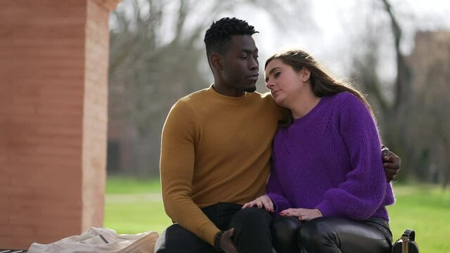 Young interracial couple at park bench kissing. Diversity concept, romantic moment together