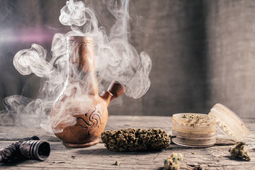 On the wooden surface is an old clay bong with medical marijuana that is smoking