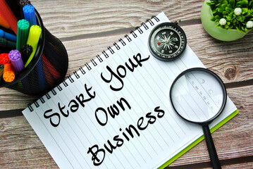 Magnify glasses, compass, colorful pen and notebook written with START YOUR OWN BUSINESS. Business, financial, self-employees, online business concept during covid-19. Selective focus.