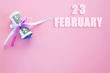 calendar date on pink background with rolled up dollar bills pinned by pink and blue ribbon with copy space. February 23 is the twenty-third day of the month