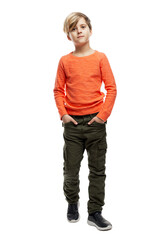 A 9-year-old boy in an orange sweater and green trousers stands with his hands in his pockets. Education and success. Isolated on white background. Vertical. © Анна Демидова
