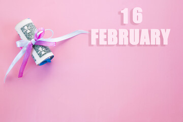 calendar date on pink background with rolled up dollar bills pinned by pink and blue ribbon with copy space. February 16 is the sixteenth day of the month