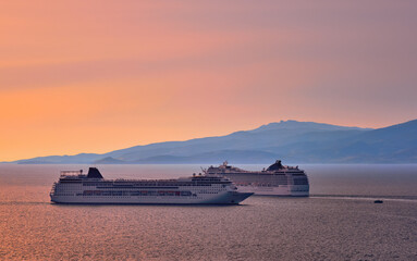 Obraz premium Two big tourist cruise liners manoeuvre in harbor. Beautiful sunset sky and distant hazy islands. Sea voyage, comfort, adventure, romantic honeymoon.