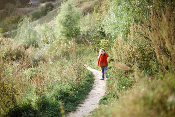 happy caucasian girl in red coat walking the trail in the park, concept autumn and happy free childhood, child safety