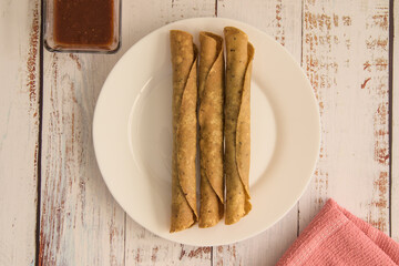 Traditional Mexican food, golden meat tacos (flautas) with red sauce.