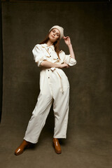 a woman in a light jumpsuit on a brown background full growth tilted her head to the side and fashionable boots