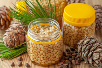 Pine nut with honey in a transparent jar. The jar is open. Nearby are pine nuts, cones and needles....