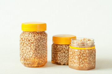 Pine nut with honey In a transparent jar with a yellow lid. Nearby are jars of nuts and honey. Place for a label. Close-up. Light background.
