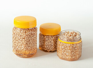 Pine nut with honey In a transparent jar with a yellow lid. Nearby are jars of nuts and honey. Place for a label. Close-up. Light background.