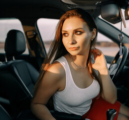 Beautiful young girl driving a car in the evening in the sunset sun on an empty parking lot