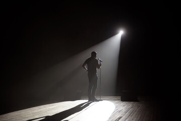 Stand up comedian on stage in the beam of light. - obrazy, fototapety, plakaty