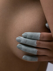 Close-up beauty of female breast covered with fingers in clay. Art photography. Clay for body and face. Clean skin, gentle care