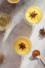  Turmeric, golden milk with lemon, spoon with turmeric powder, honey on grey background. Alternative medicine concept.