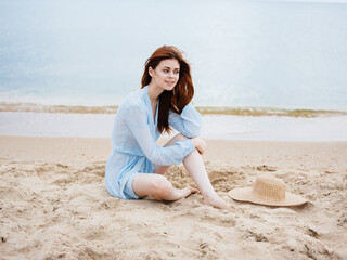 Fototapeta na wymiar happy woman in transparent blue dress sits on the sand near the sea