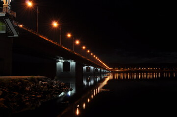 Night view of the bridge over the Kola river. The city of Murmansk. A long bridge with illuminated lanterns reflecting in the water. Murmansk region, Russia