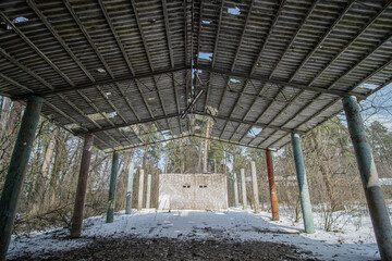 Old dilapidated canopy of abandoned territory in a coniferous forest in winter on a sunny day. The ruins of a former open-air cinema of a devastated children's camp.