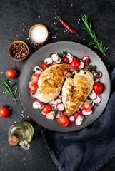Grilled chicken breast and salad with fresh vegetables, tomatoes and radishes in a plate Chicken meat with salad. Healthy food on stone background