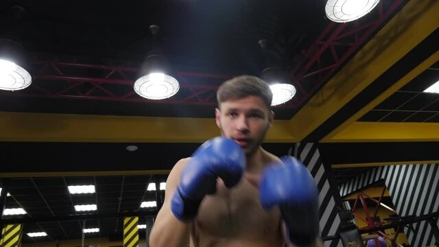 Portrait of a young muscular guy in blue boxing gloves in the gym.