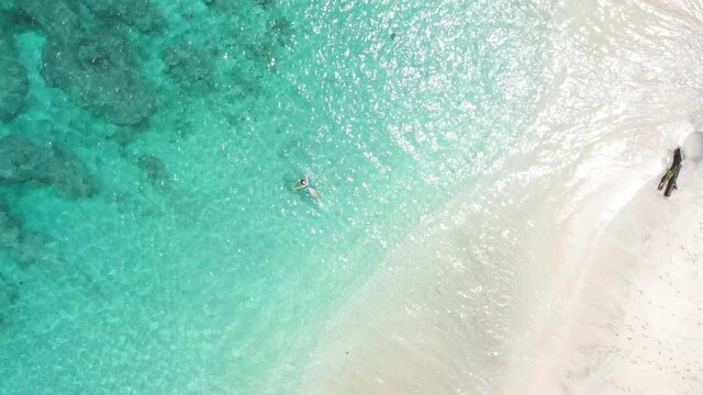 top view of the beautiful blue azure water in the center of the frame a girl enjoying warm water surrounded by white sand and tropical vegetation