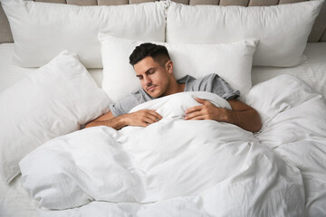 Handsome man sleeping under soft blanket in bed at home, above view