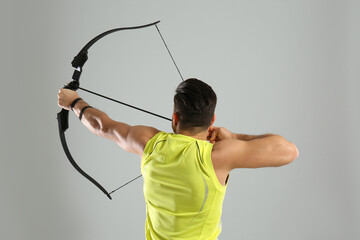 Man with bow and arrow practicing archery on light grey background, back view