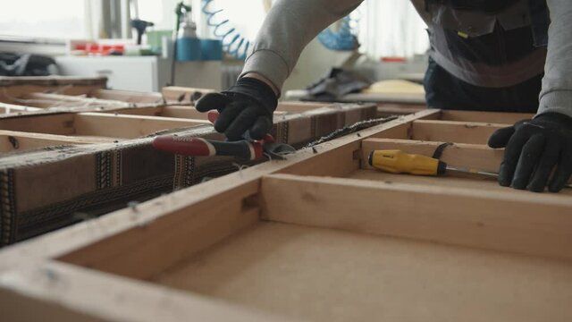 Misk, Belarus - May 15, 2020: A man in black gloves works in a furniture repair workshop and pulls out staples from the wooden frame of an old sofa