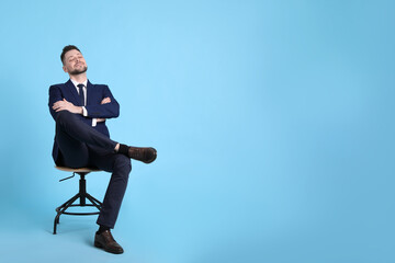 Handsome businessman relaxing in office chair on light blue background