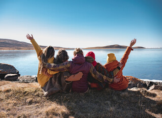 Group of happy friends sitting at mountain lake