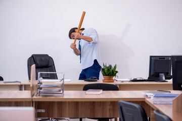 Young male furious employee holding baseball bat in the office
