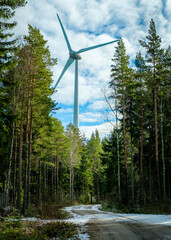 Wind turbine natuarally framed by trees with a snow covred road leading to it. At hjo, sweden